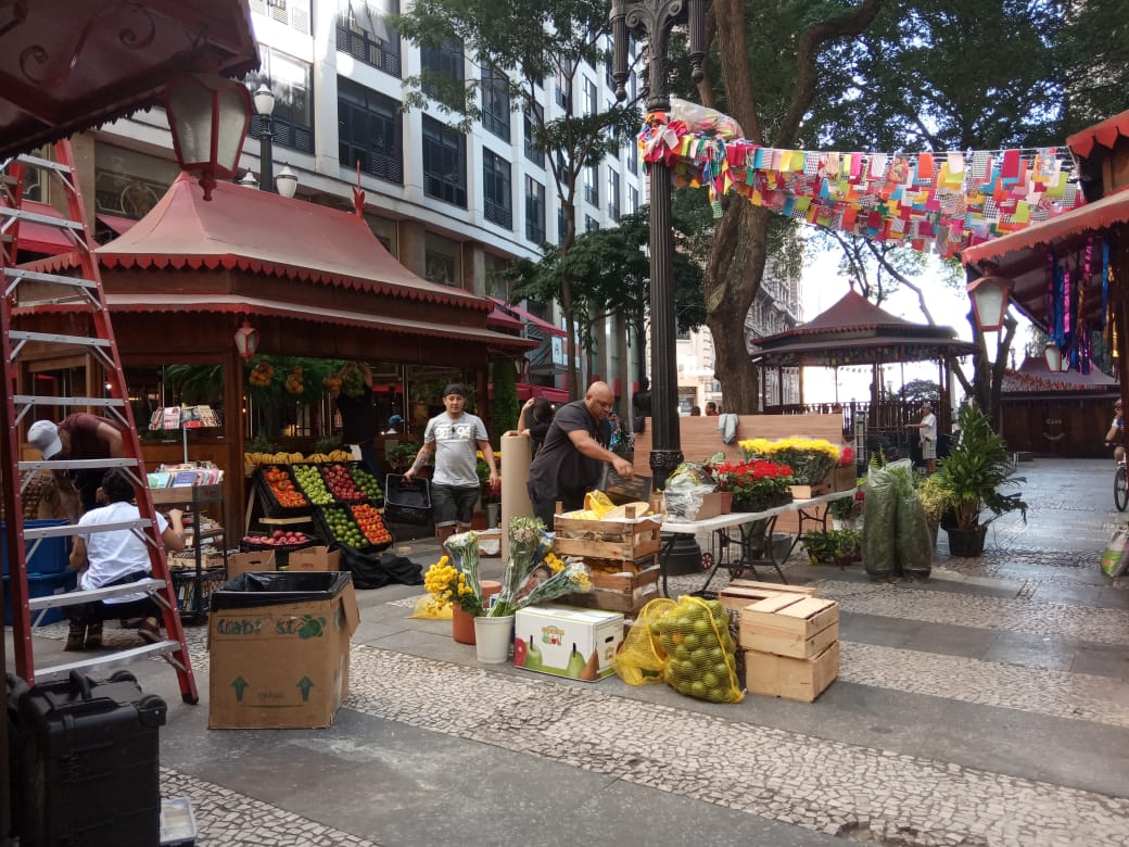 Funcionários organizando feira de frutas e flores.